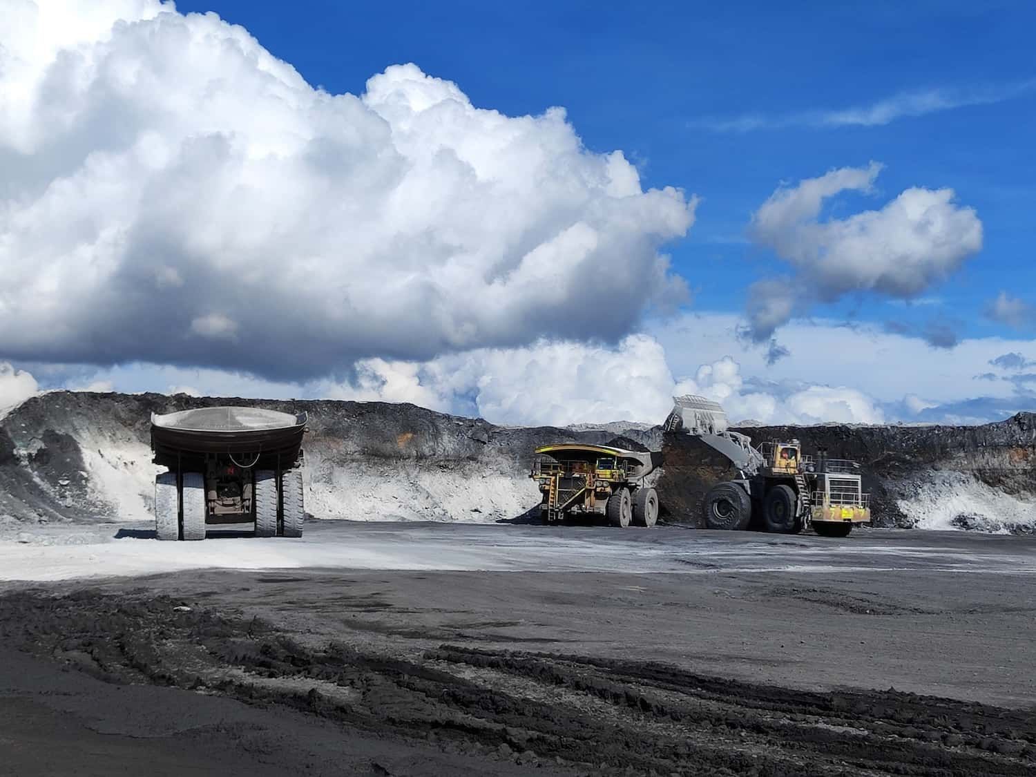 Industrial vehicles on an open extraction landscape beneath bright clouds.