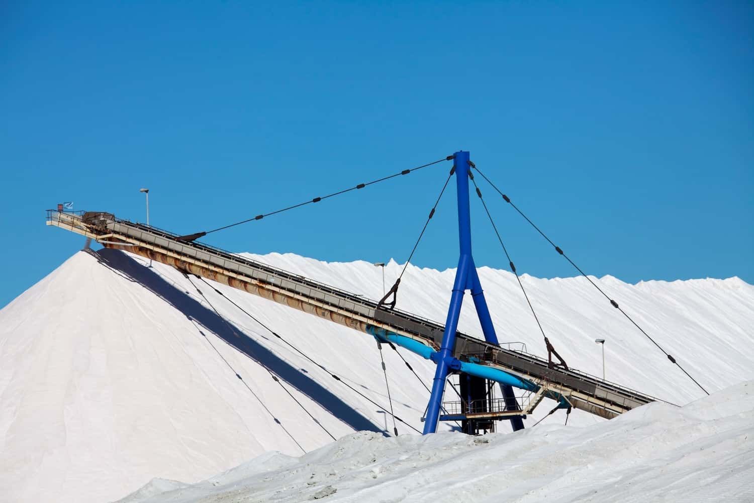 White aggregate piles and industrial infrastructure under a clear blue sky.